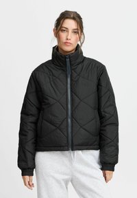 Giacca a vento nera trapuntata con colletto alto, zip anteriore completa, polsini elastici e silhouette cropped. Finitura opaca con texture.