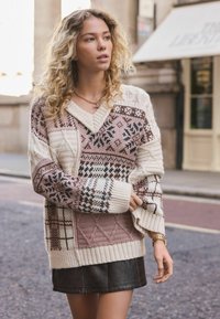 Knit sweater featuring a mix of soft beige, pink, and black patterns, with a v-neckline and ribbed cuffs, paired with a dark leather skirt.