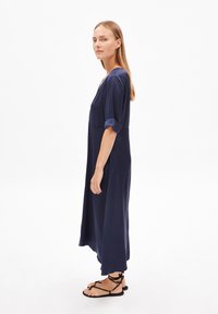 Marinblå knälång klänning i ett mjukt tyg, med V-ringning, lösa ärmar och avslappnad passform. Matchas med svarta sandaletter med remmar.