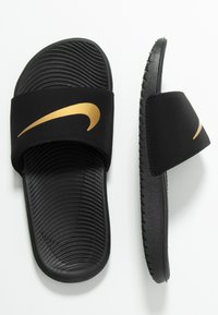 Sorte badesandaler med en struktureret sål, gummistrop og et fremtrædende Nike swoosh-logo i guld. Flad design til afslappet brug.