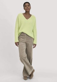 Limettengrüner, gerippter Strickpullover mit V-Ausschnitt; kombiniert mit beigen Cordweitenhosen und beigen Schuhen. Schlichte, entspannte Passform.