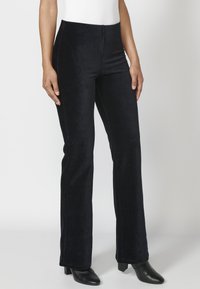 Zwarte velours flare-broeken met een gladde textuur, minimale naden en een hoge tailleband. Gecombineerd met zwarte hakken.