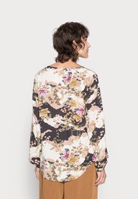 Blusa floral em tecido leve com mangas longas, apresentando um padrão multicolorido de flores rosas e douradas num fundo preto.