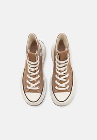 Braune Canvas-Hochtop-Sneaker mit weißen Schnürsenkeln und Gummisohlen. Mit einem schwarzen Streifen entlang der Sohle und einer runden Zehenkappe.