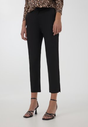 Czarne tapered trousers o gładkiej strukturze, z bocznymi rozcięciami na dole, w połączeniu z czarnymi sandałkami na obcasie i bluzką w panterkę.