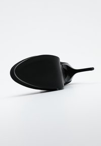 Svart högklackad sko med spetsig tå, slät yta och en något böjd, räfflad design på sulan. Elegant och glansig finish.