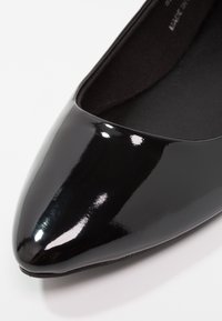 Gros plan d'une chaussure plate noire en cuir verni à bout pointu avec une surface lisse et brillante et une doublure intérieure noire.