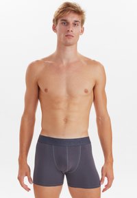 Pantaloni boxer in cotone grigi con una cintura goffrata con logo, caratterizzati da una vestibilità aderente e un design a vita media, texture liscia e senza motivi visibili.