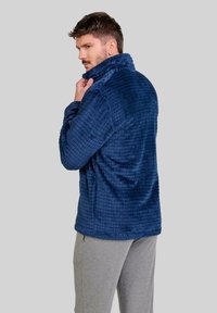 Chaqueta de forro polar texturizada de color azul marino con un collar alto y un patrón de cuadrícula. Presenta bolsillos laterales y un ajuste relajado.