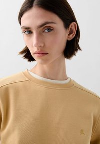 Geel sweatshirt met een ronde halslijn en geribbelde afwerking, met een klein geborduurd logo op de borst en een gestructureerde stof.