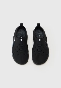 Černé nazouvací boty s hladkým povrchem, texturovanými akcenty a ventilačními otvory. Zahrnují centrální pásek a bílé logo na boku.