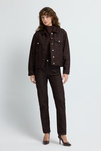 Chaqueta de mezclilla marrón oscuro con bolsillos frontales, botones de bronce y pantalones ajustados a juego en marrón oscuro. La modelo lleva tacones, contra un fondo claro.