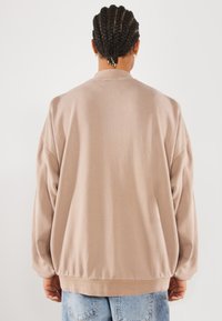 Light beige oversized sweatshirt with a round neckline and long sleeves, featuring ribbed cuffs and hem. Soft fabric texture.