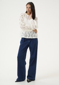 White lace long-sleeve top with intricate patterns, paired with dark blue wide-leg jeans and black pointed-toe heels.