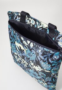 Floral tote bag in navy with blue and cream patterns. Features zip closure and contrasting handles. Material appears smooth and durable.