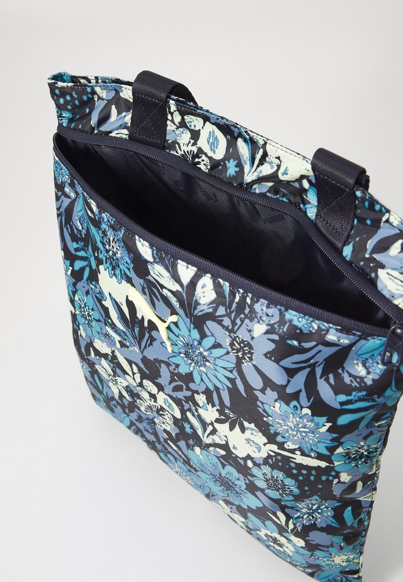 Bloemen schoudertas in navy met blauwe en crèmekleurige patronen. Voorzien van een ritssluiting en contrasterende handvatten. Het materiaal lijkt glad en duurzaam.