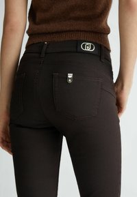 Bruine denimjeans met een slim fit, voorzien van achterzakken en een klein zilverkleurig hardwareaccent op de rechterszak.