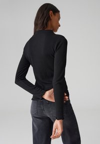 Schwarzes, geripptes Langarmoberteil mit hohem Kragen, tailliertem Oberteil und Rüschensaum, kombiniert mit dunkelgrauen Jeans. Glatte, dehnbare Textur.