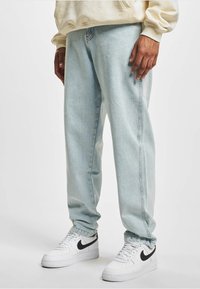 Jeans din denim bleu deschis cu o croială relaxată, cu cusături laterale, picioare drepte și asortați cu adidași albi cu accente negre.