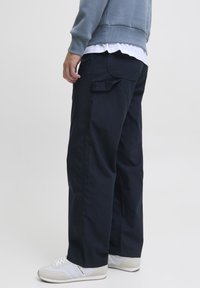 Pantaloni cargo blu navy con vestibilità rilassata, dotati di una tasca posteriore e dettagli cuciti, abbinati a scarpe da ginnastica bianche.