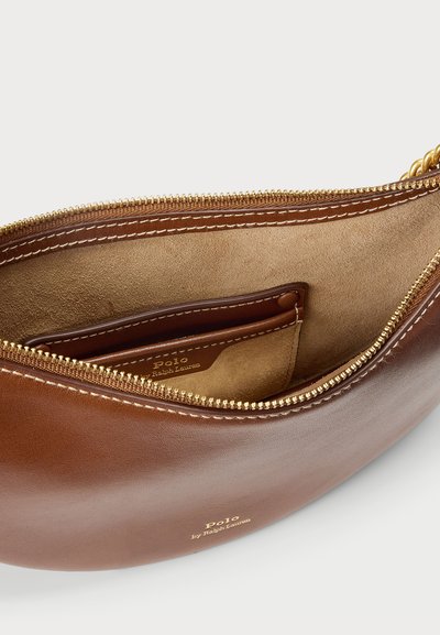 Ruda odinė rankinė su apvalia forma ir auksine užtrauktuku. Minkšta vidinė dalis su kortelių lizdais. Logotipas įspaustas ant išorės.