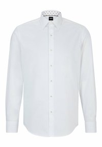Chemise blanche à manches longues avec un col pointu et un motif à pois subtil à l'intérieur du col. Dotée de boutons dorés et de poignets doubles.