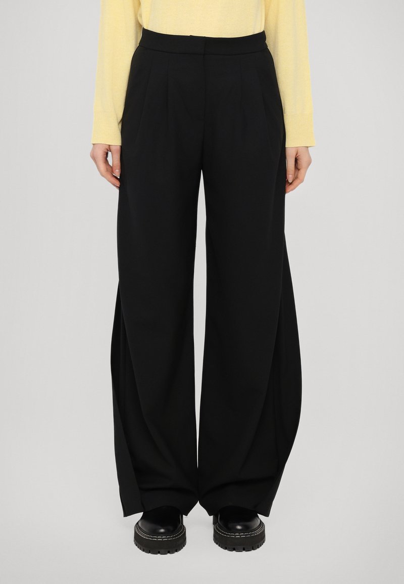 Pantalones negros de pierna ancha con pliegues, confeccionados en una tela suave. El diseño presenta una cintura alta y una silueta alargada.
