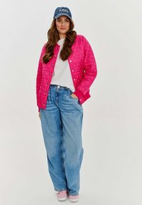 Prešívaná ružová bunda s cvokmi, kombinovaná s bielym tričkom a voľnými svetlomodrými džínami. Na hlave má námornícku baseballovú čiapku a ružové tenisky.