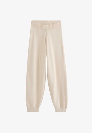 Kvinde iført lysebeige bukser med vide ben og høj talje, kombineret med en sort top, hænderne hviler ned langs siderne.