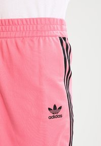 Růžové šortky Adidas z bavlny s elastickým páskem. Mají černé třípruhové detaily a malou černou značku na levé straně.