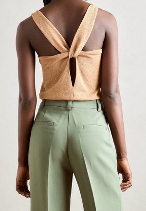 Beige gebreide top met een gedraaide achterkant en een sleutelgatopening, gecombineerd met groene getailleerde broek met zijzakken.