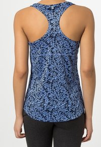 Mujer vistiendo una camiseta deportiva sin mangas con espalda de corredor y un patrón abstracto azul y negro, combinada con mallas negras, vista desde atrás.