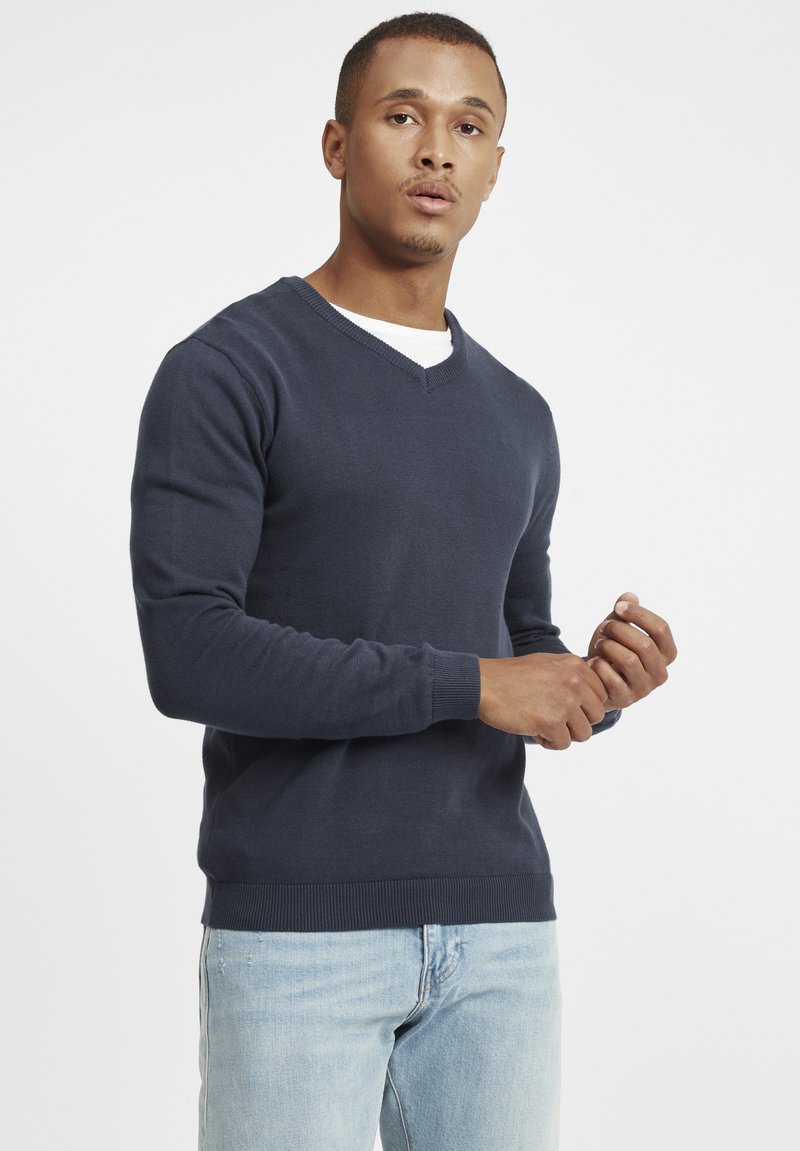 Maglione blu navy con scollo a V, polsini e orlo a coste, realizzato in maglia, abbinato a jeans azzurri.