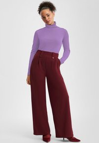 Długie burgundowe spodnie o szerokich nogawkach z podwójnymi guzikami, zestawione z dopasowanym fioletowym golfem z długim rękawem. Miękka faktura, przemyślana konstrukcja.
