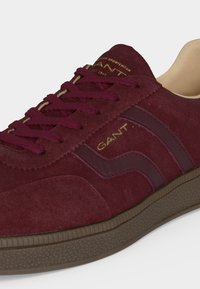 Μπορντό δερμάτινο sneaker από σουέτ με σκούρες δερμάτινες λεπτομέρειες στα πλαϊνά, κορδόνια που ταιριάζουν, ταμπά εσωτερική επένδυση, υφασμένο καφέ λαστιχένιο πέλμα και χρυσή επωνυμία "GANT".