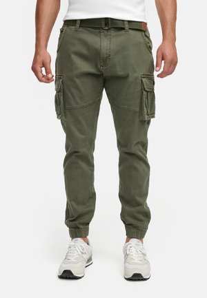 Man wearing olive green cargo pants with elastic cuffs and a green belt, paired with white sneakers.