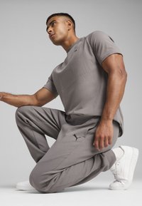 Šedý sportovní outfit skládající se z trička s krátkým rukávem a tapered kalhot, doplněný bílými teniskami. Obsahuje černou logo detaily na oblečení.
