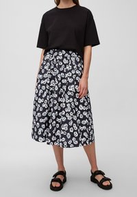 Camiseta negra combinada con una falda floral hasta la rodilla con fondo azul marino, flores blancas y azules, y un diseño plisado. Sandalias negras.