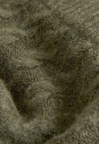 Tissu tricoté doux de couleur vert olive avec une texture duveteuse et des boucles visibles, drapé avec des plis et des ombres naturelles.