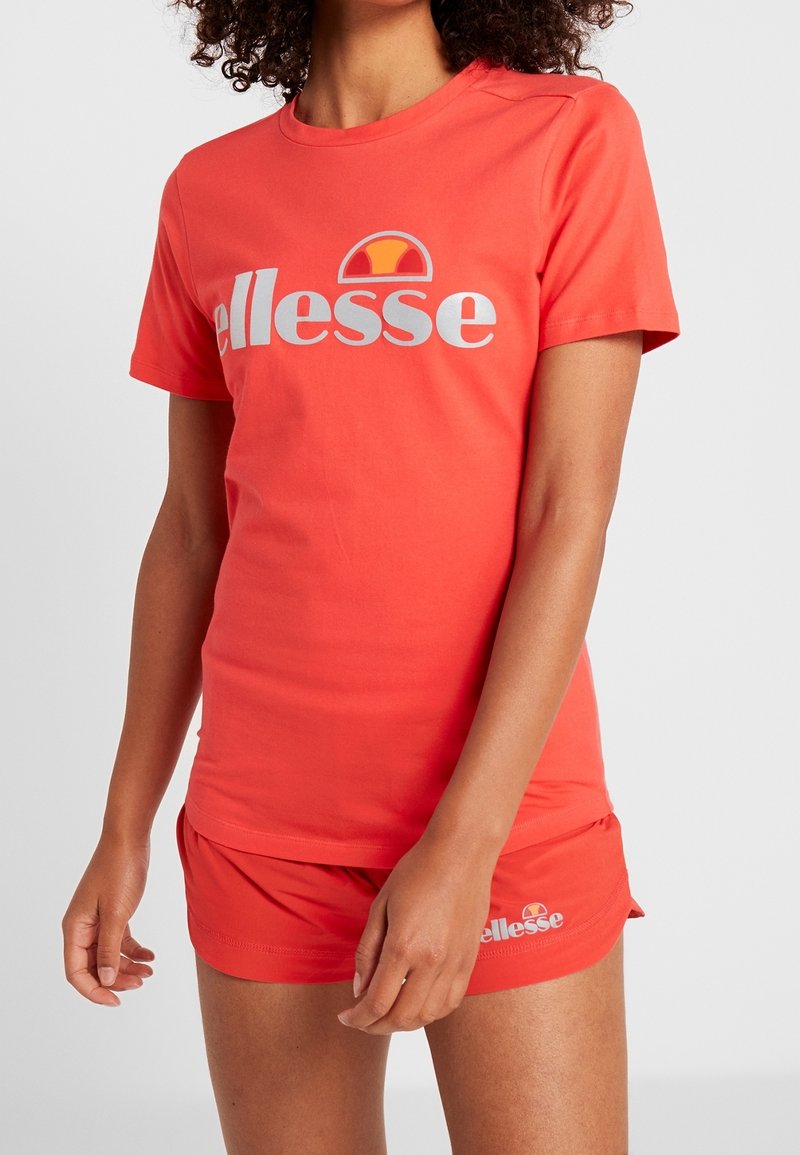 T-shirt en coton rouge à col rond et manches courtes, avec un logo blanc et un motif de soleil sur la poitrine. Porte avec un short assorti.