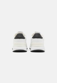 Sneakers bianche con accenti neri sui talloni, parte superiore in materiale sintetico, suola ammortizzata e dettaglio del logo sul retro. Suola in gomma testurizzata.