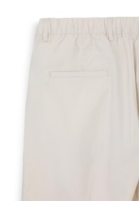 Pantaloni beige chiaro con vita elastica, dotati di una tasca posteriore singola con una delicata cucitura e una texture liscia e morbida.