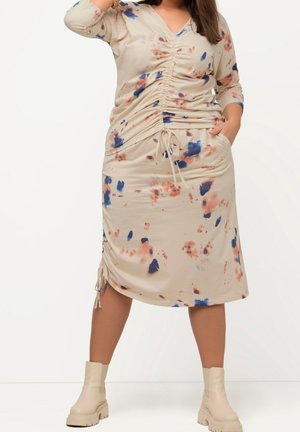 Beżowa sukienka z niebieskim i koralowym wzorem w plamki, marszczeniem po bokach, dekoltem w kształcie litery V, rękawami do połowy przedramienia oraz regulowanymi trokami na dole.