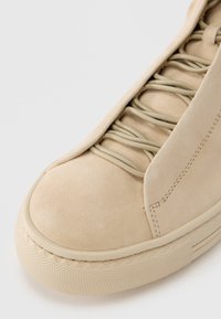 Μπεζ δερμάτινο αθλητικό παπούτσι με στρογγυλή μύτη, διαθέτει ελαστικά κορδόνια και υφασμένο καουτσούκ σόλα, λείο πάνω μ έρος με διακριτικές λεπτομέρειες ραφής.