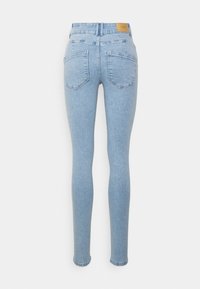 Jeans justos de cor azul claro com cintura alta, design de cinco bolsos e um patch de couro na parte de trás. Textura de denim suave com ligeira elasticidade.