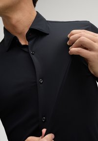 Schwarzes, tailliertes Hemd mit Knöpfen aus glattem Stoff und spitzem Kragen. Verfügt über schwarze Knöpfe und ist am Kragen leicht aufgeknöpft.