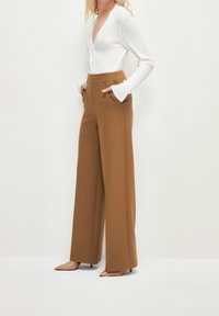 Haut blanc à manches longues côtelé associé à un pantalon marron taille haute à jambes larges. Le pantalon comporte des poches sur les côtés et une texture lisse.