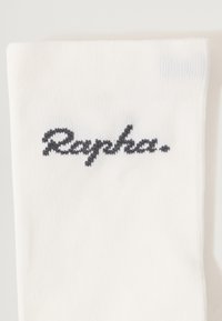 Hvid sok lavet af struktureret stof med et grått, broderet "Rapha." logo. Enkel, ren design uden yderligere mønstre eller accenter.