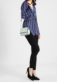 Stribet bluse i marineblå og hvid, med bælte i taljen, parret med sorte strukturerede bukser og sorte stiletto hæle. Lyseblå crossover taske.