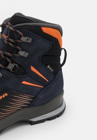 Herren Wanderschuh aus marineblauem Wildleder und Mesh. Mit orangefarbenen Akzenten, strukturierten Oberflächen, Gummisohle und GORE-TEX-Label für Wasserdichtigkeit.